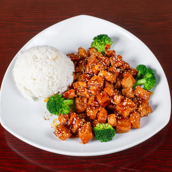 Sweet and sour chicken with white rice and broccoli florets on a white plate.