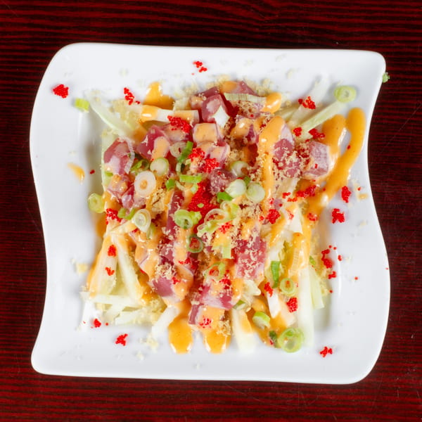 A vibrant poke salad with tuna, green onions, and orange sauce, topped with red roe on a white plate.