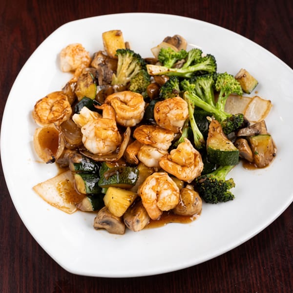 Shrimp and mixed vegetables, including broccoli, zucchini, onions, and mushrooms, on a white plate.
