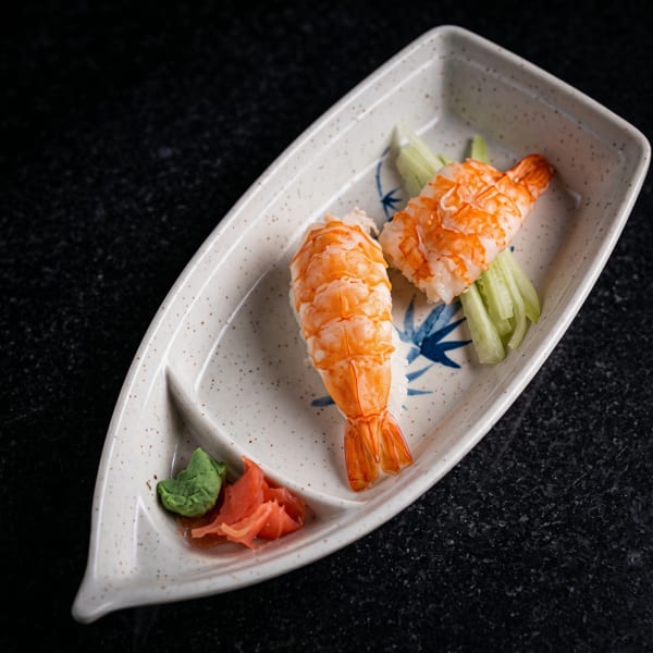 Two shrimp nigiri sushi pieces with wasabi and pickled ginger on a boat-shaped plate.