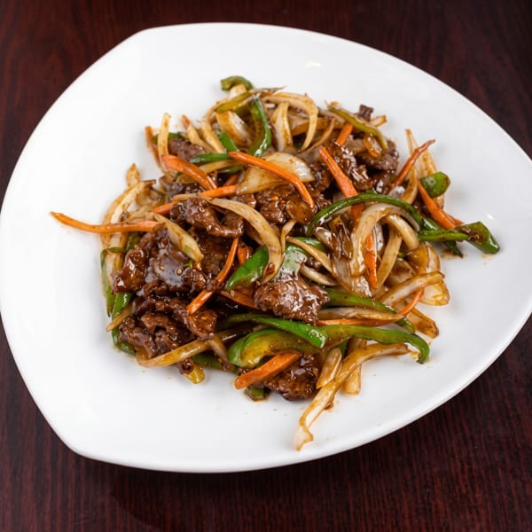 Stir-fried beef with sliced onions, green peppers, and carrots on a white plate.