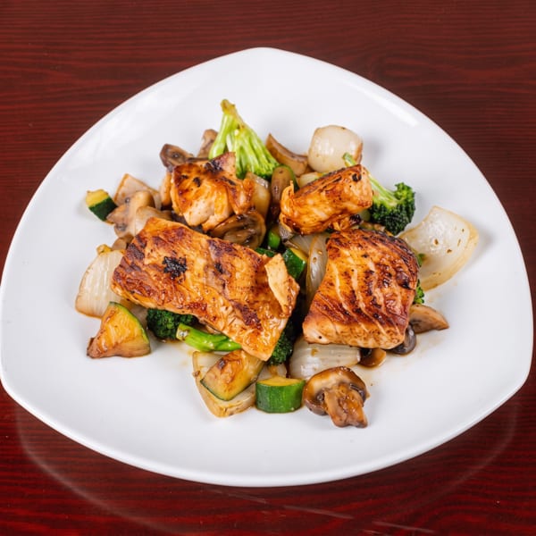 Grilled salmon pieces with sautéed broccoli, zucchini, mushrooms, and onions on a white plate.