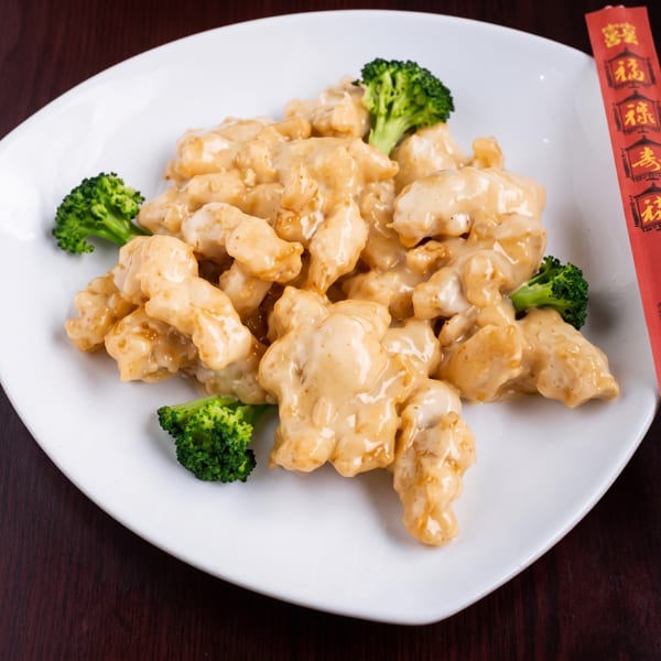 Creamy orange chicken with broccoli florets on a white plate, with red chopsticks on the side.