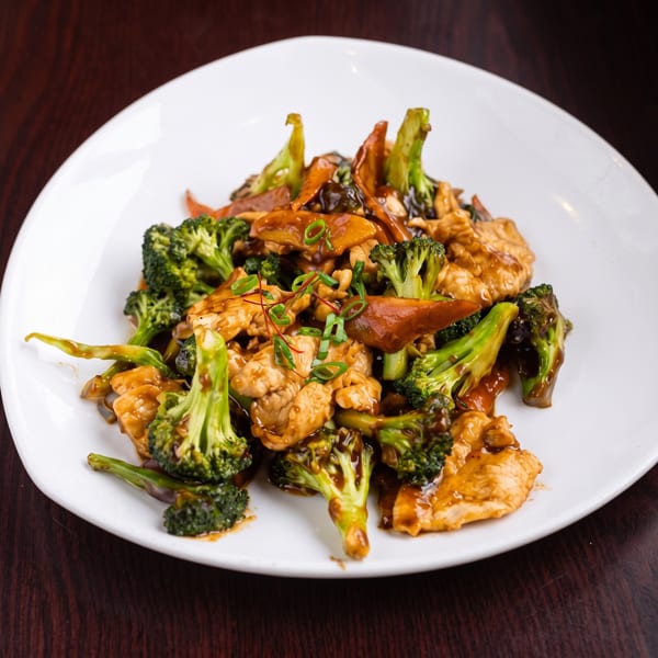 Chicken and broccoli stir-fry with mushrooms and green onions on a white plate.