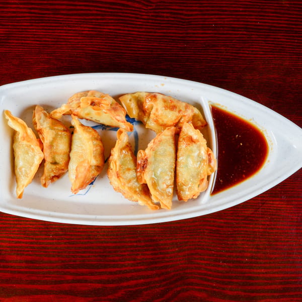 A white boat-shaped plate holds golden-brown fried dumplings and a section of dark dipping sauce.
