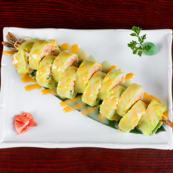 Sushi rolls with light green and orange sauce, garnished with pickled ginger and wasabi.