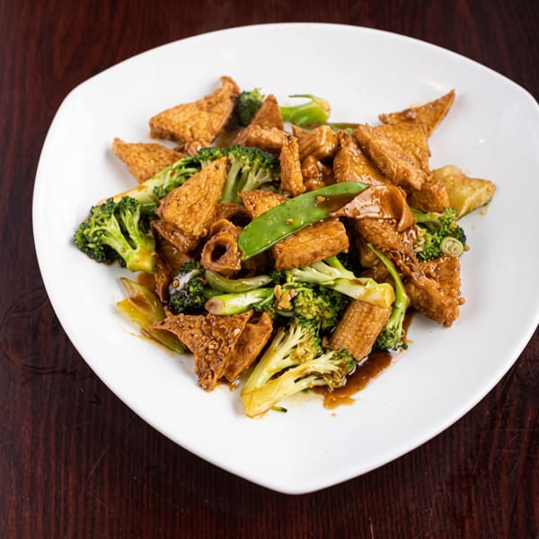 Tofu and broccoli stir-fry with snow peas and baby corn in a savory sauce on a white plate.